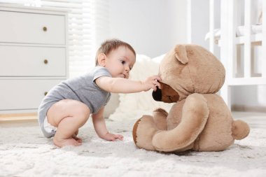 Küçük şirin bebek odada oyuncak ayıyla oynuyor.