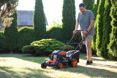 Bahçede çim biçme makinesiyle yeşil çim biçen bir adam