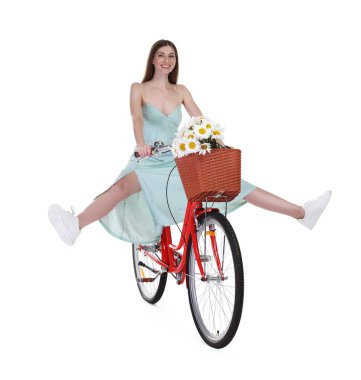 Gülen kadın, beyaz arka planda çiçek dolu bir sepetle bisiklet sürüyor.
