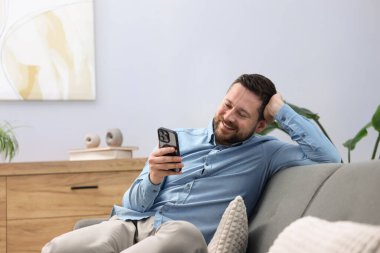 Adam evde akıllı telefondan bir şey izlerken gülüyor.