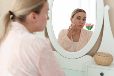 Evde aynaya bakan sivilceli bir kadın.