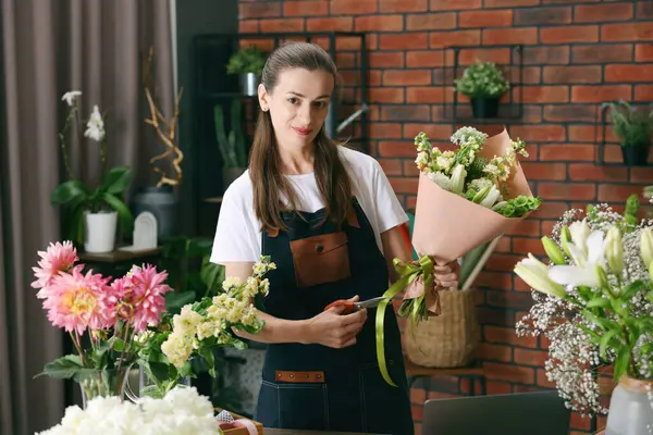 Profesyonel çiçekçi dükkandaki ahşap masada çiçek buketi yapıyor.