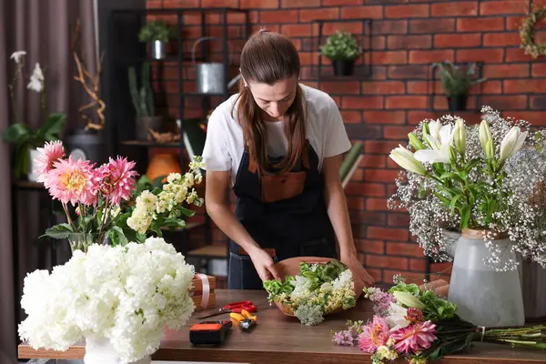 Profesyonel çiçekçi dükkandaki ahşap masada çiçek buketi yapıyor.