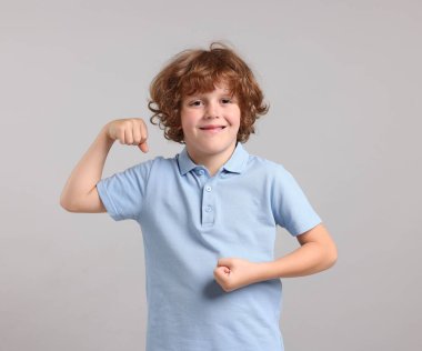 Kuvvet. Küçük mutlu çocuk açık gri arka planda pazılarını gösteriyor.