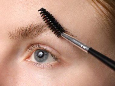 Genç bir kadın kaşlarını hortlakla fırçalıyor, yakın plan.