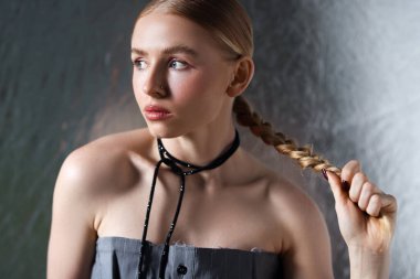 Metalik arka planda poz veren at kuyruklu güzel kadın.