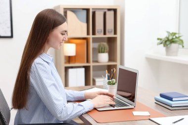 İçerideki ahşap masada dizüstü bilgisayar kullanan metin yazarı