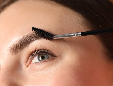 Genç bir kadın kaşlarını hortlakla fırçalıyor, yakın plan.