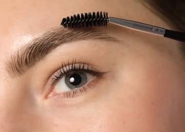 Genç bir kadın kaşlarını hortlakla fırçalıyor, yakın plan.