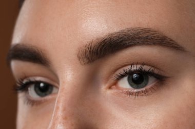 Kahverengi arka planda güzel kaşları olan genç bir kadın, yakın plan.