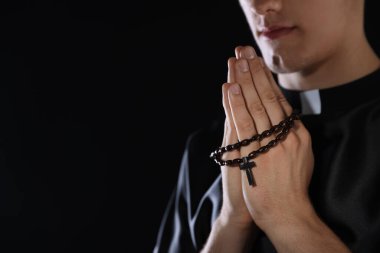 Karanlık arka planda tespih çeken bir rahip, yakın plan. Metin için boşluk