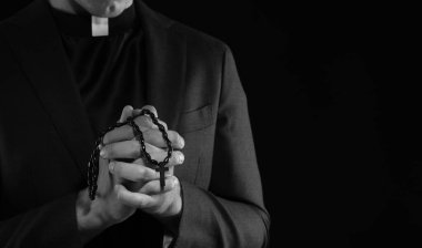 Karanlık arka planda tespih çeken bir rahip, yakın plan. Siyah ve beyaz etkisi