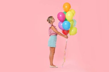 Güneş gözlüklü gülümseyen kadın pembe arka planda bir demet renkli balonla