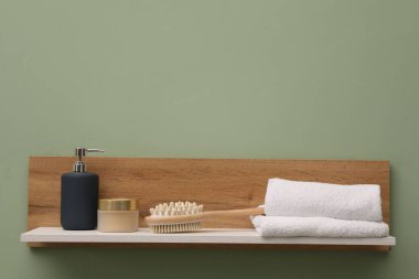 Açık yeşil duvarda havluları, fırçası ve kozmetik ürünleri olan beyaz ahşap raf, metin için yer