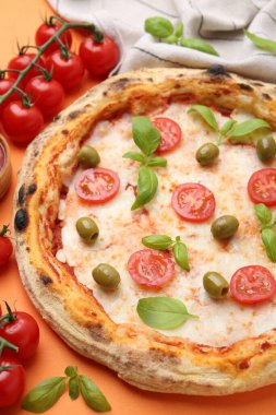 Turuncu arka planda domatesli, fesleğenli ve zeytinli lezzetli pizza, yakın plan.
