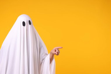 Hayalet kostümlü adam turuncu arka plandaki bir şeyi işaret ediyor. Metin için boşluk