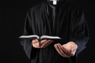 Kutsal İncil 'i olan ve siyah arka planda vaaz veren bir rahip, yakın plan.