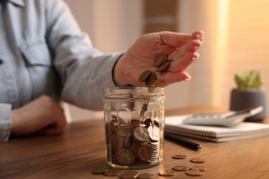 Ahşap masada kavanoza bozuk para koyan kadın, yakın plan.