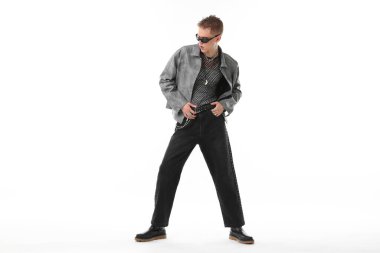 Beyaz arka planda şık ceket ve güneş gözlüğü takan yakışıklı bir genç.