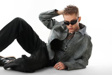 Beyaz arka planda şık ceket ve güneş gözlüğü takan yakışıklı bir genç.