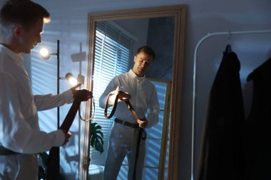 Kapalı alanda aynanın yanında kravat seçen bir adam.