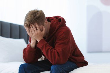 Evde elleri yatakta olan üzgün adam yüzünü kapatıyor. Depresyon