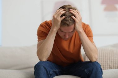 Evdeki kanepede oturan üzgün adam.