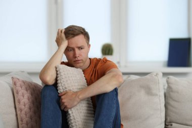 Evdeki kanepede üzgün, düşünceli bir adam.