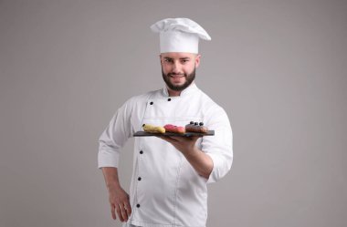 Üniformalı mutlu pastacı açık gri arka planda lezzetli ekinler tutuyor.