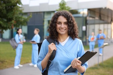 Sırt çantası, not defteri ve not defteri açık havada seçici bir odak noktası olan üniformalı bir tıp öğrencisi.