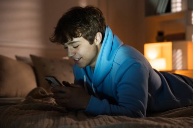 Evde akıllı telefon kullanan gülümseyen genç çocuk.