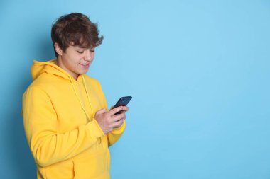 Açık mavi arka planda akıllı telefon kullanan gülümseyen genç çocuk. Metin için boşluk