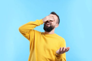 Gözleri kapayan ve açık mavi arka planda gülen adam.