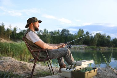 Yazın sandalyede oturan ve göl kenarında balık tutan oltalı balıkçı.