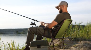 Yazın sandalyede oturan ve göl kenarında balık tutan oltalı balıkçı.