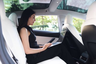 Modern arabada dizüstü bilgisayar kullanan bir kadın. Dışarıdan görünüyor.