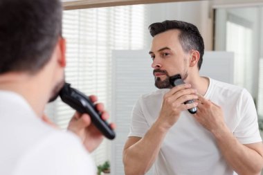 Yakışıklı adam evde aynanın yanında tıraş makinesiyle tıraş oluyor.