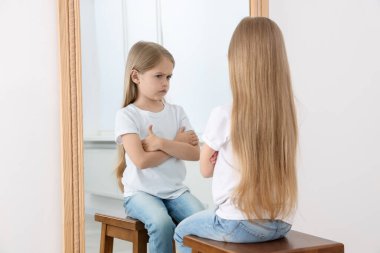 Üzgün küçük kız aynada kendine bakıyor.