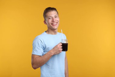 Sarı arka planda serinletici içecek dolu kavanozu olan mutlu adam.