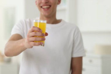 Evde elinde bir bardak portakal suyuyla gülümseyen adam, yakın plan. Tazeleyici içecek.