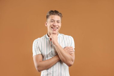 Hayaller gerçek oluyor. Kahverengi arka planda bir şeyler düşünen pozitif genç adam.