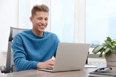 İçerideki ahşap masada dizüstü bilgisayar kullanan metin yazarı