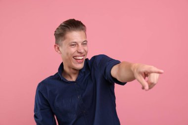 Yakışıklı adam gülüyor ve pembe arka plandaki bir şeye işaret ediyor. Pozitif duygu