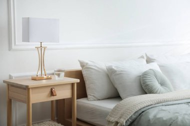 Yatak odasının yanında lamba ve bir bardak su olan komodinin yanında.