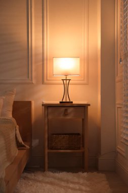 Yatağın yanında lamba olan komodin.