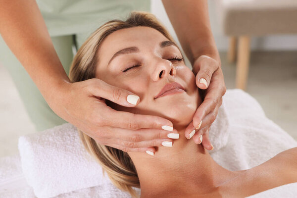 Красивая женщина получает массаж лица на диване в помещении, крупным планом