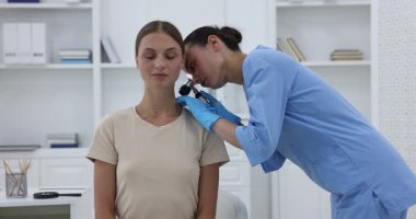 Doktor hastanede dermatoskopla genç kadının benini inceliyor.