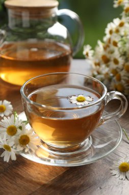 Cam bardakta romatik çay ve ahşap masada papatya çiçekleri, yakın plan.