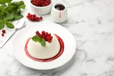 Kırmızı üzümlü lezzetli panna cotta, beyaz mermer masada sos ve nane, yakın plan.