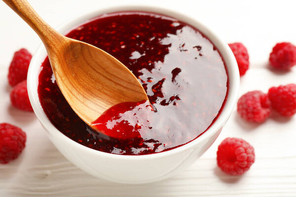 Принимая сладкое малиновое варенье ложкой из миски на белый стол, крупным планом